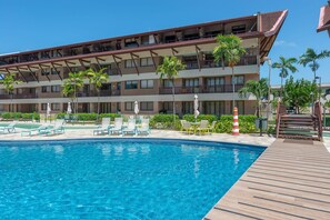 A hotel with a swimming pool, outdoor seating, and a multi-story building with balconies.
