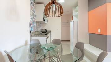 Une cuisine moderne avec une table à manger en verre, des chaises blanches et un luminaire suspendu original.