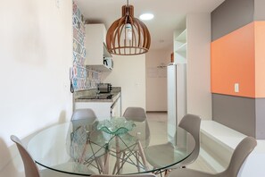 Une cuisine moderne avec une table à manger en verre, des chaises blanches et un luminaire suspendu original.