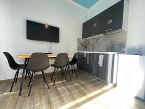 Een moderne keuken met een marmeren spatwand, een flatscreen televisie boven de counter en een eethoek met vier stoelen.