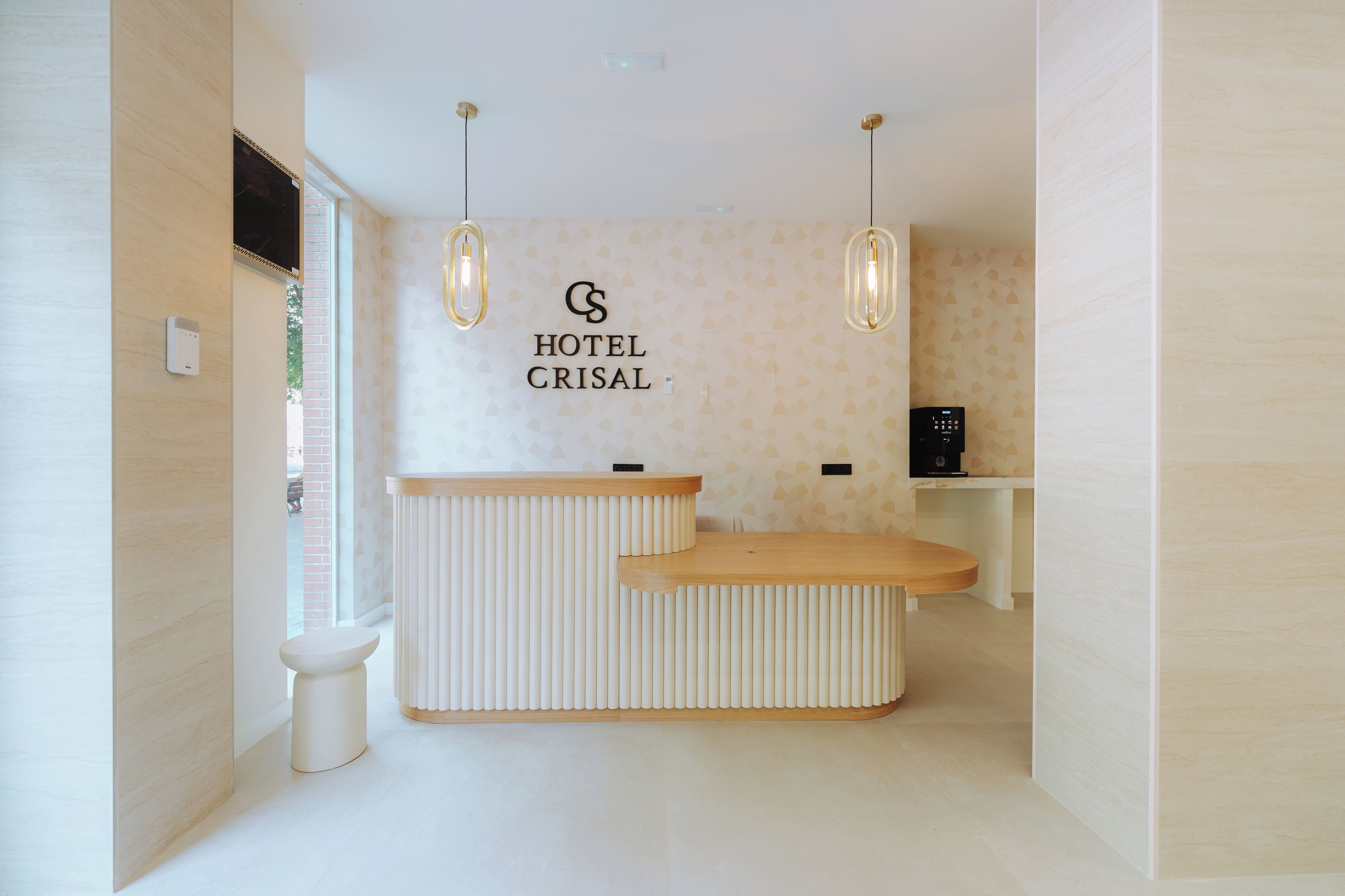 Un mostrador de recepción de hotel con diseño moderno, un letrero en la pared que dice 'HOTEL CRISAL' y una pequeña zona de estar con un pedestal blanco.