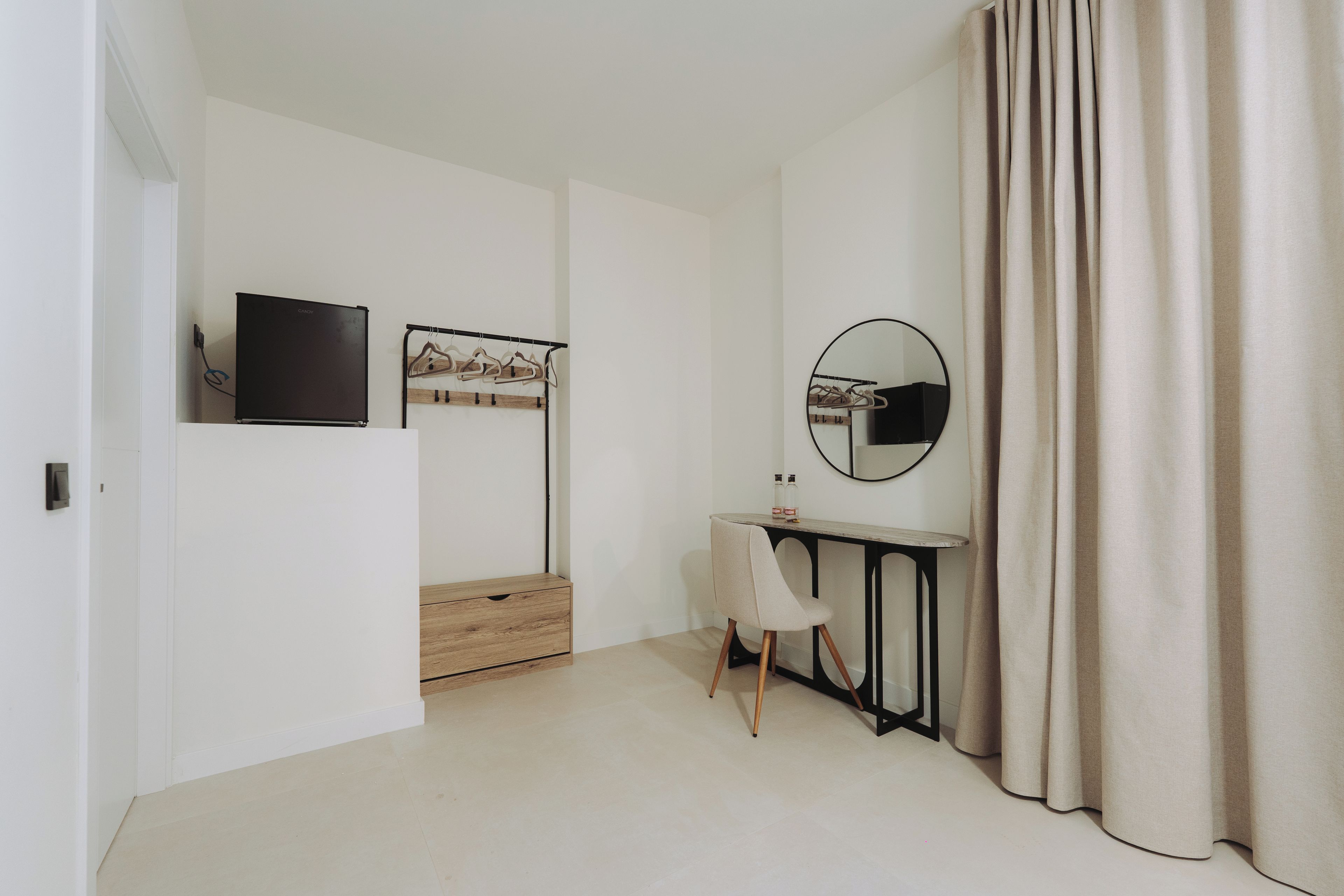 A minimalist bedroom with a bed, a bedside table, a mirror, and a TV mounted on the wall.