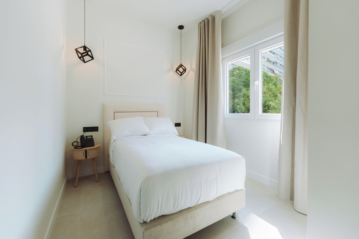 Un dormitorio con una cama, mesitas de noche, un teléfono y una ventana con cortinas.