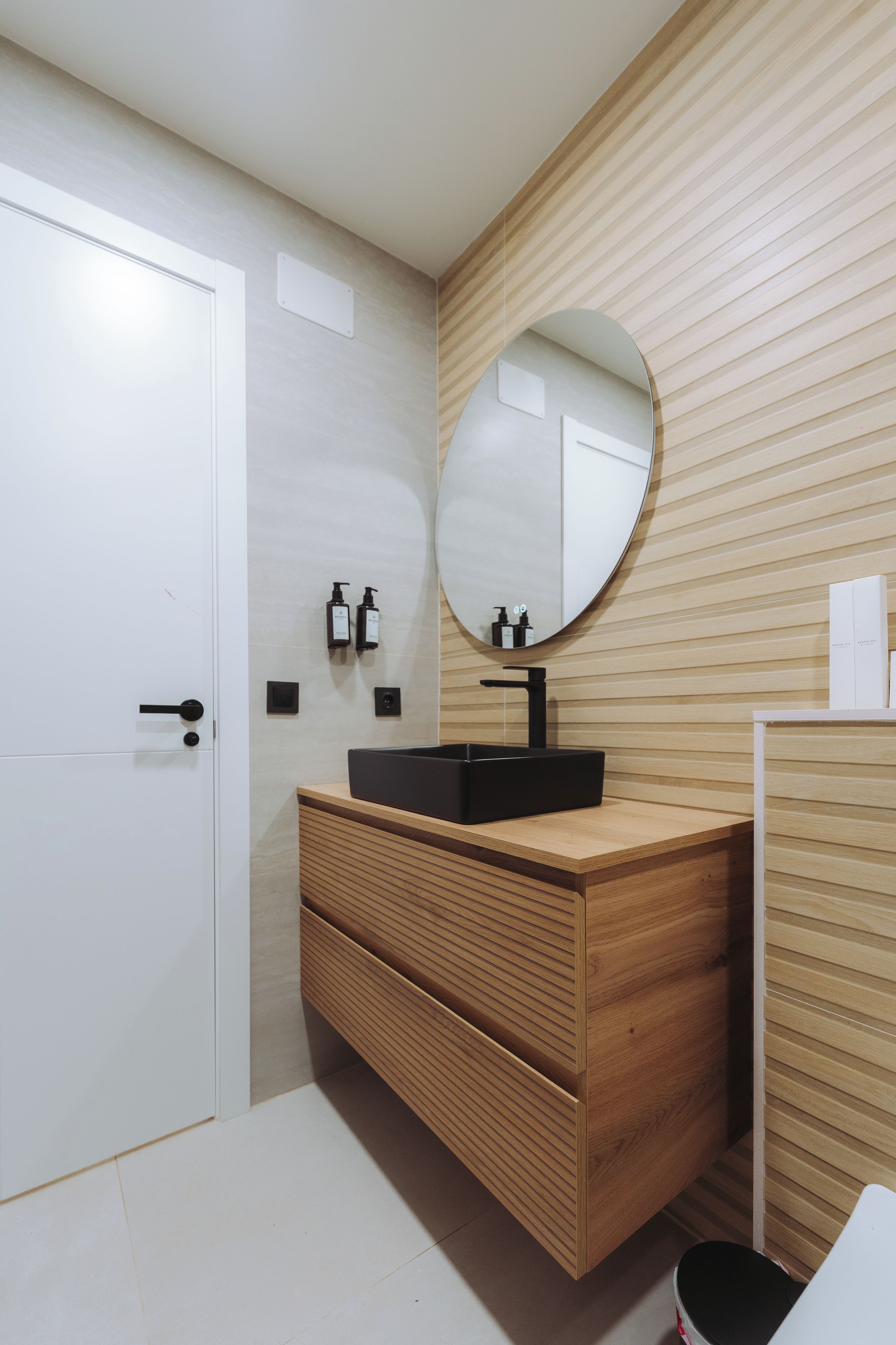 Une salle de bain moderne avec un meuble-lavabo en bois, un lavabo noir et un miroir.