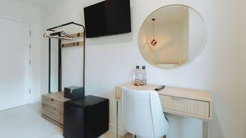 A modern bedroom with a wooden desk, a chair, a black wardrobe, a television, a mirror, and a hanging coat rack.