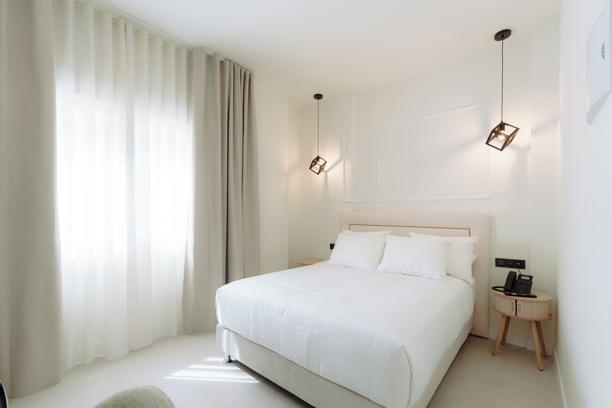 Una habitación de hotel moderna con una cama grande, una mesita de noche, una lámpara y un teléfono.