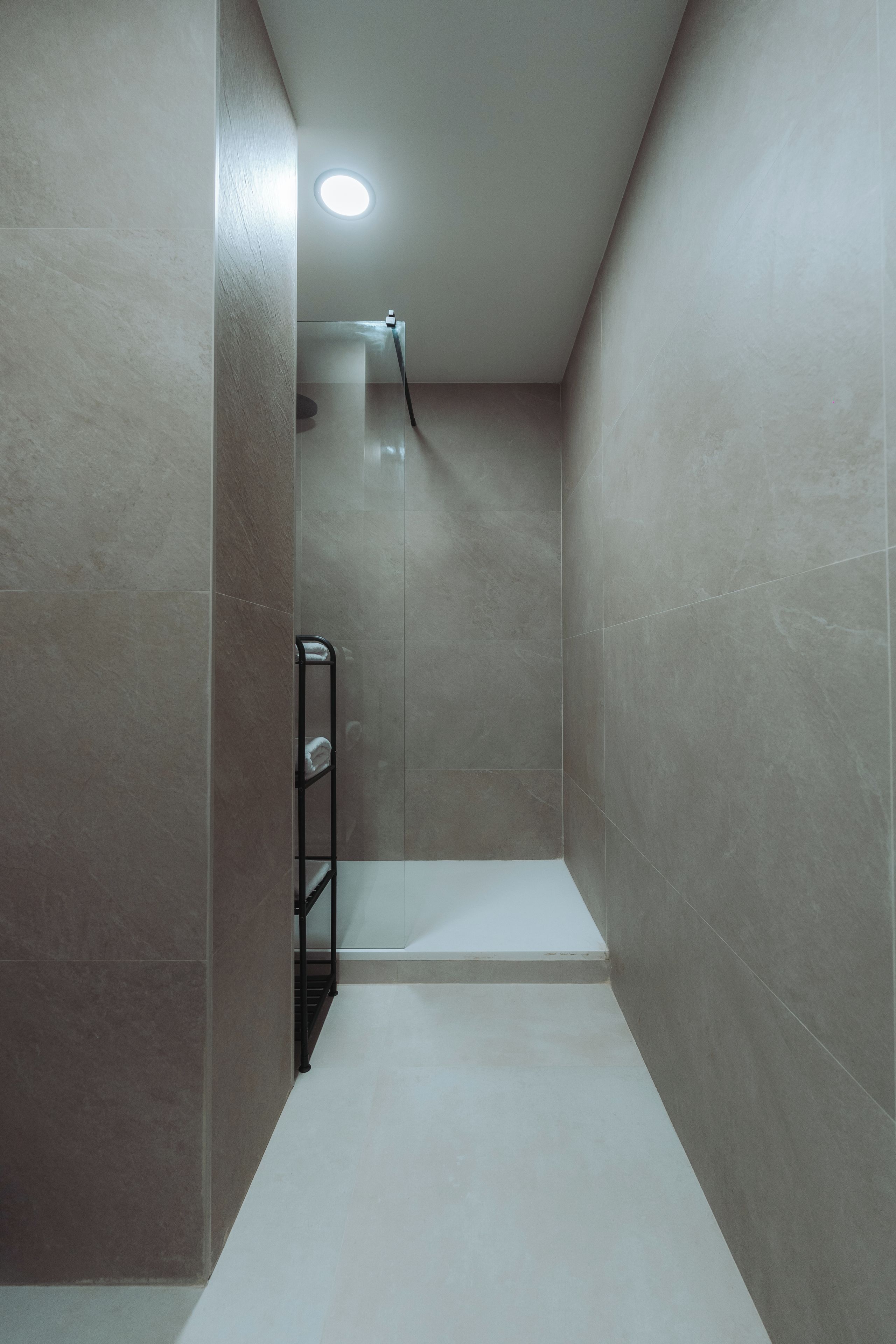 A modern shower stall with a glass door, a metal shelf, and a ceiling light.