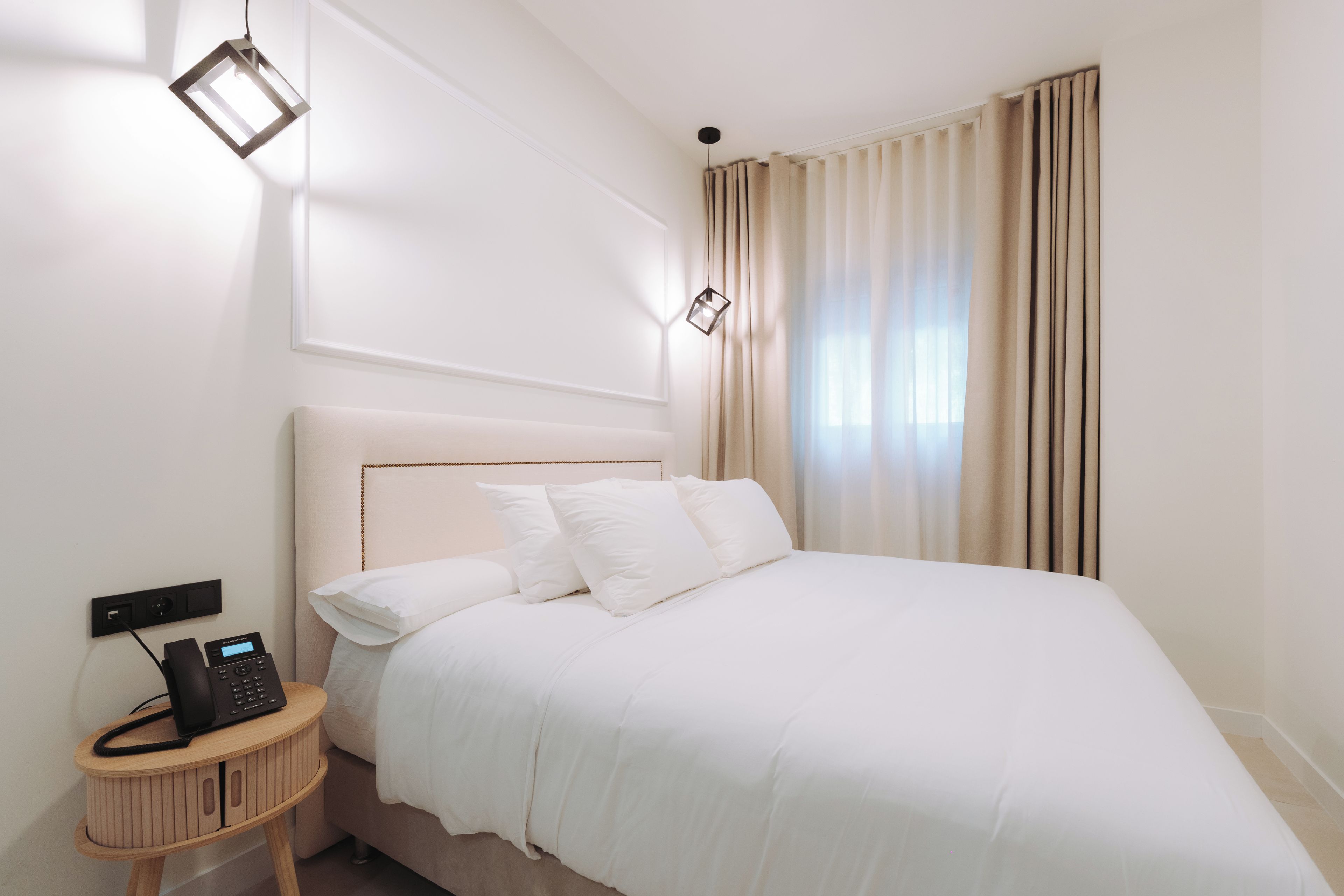 A hotel room with a bed, bedside table, and a wall-mounted phone.