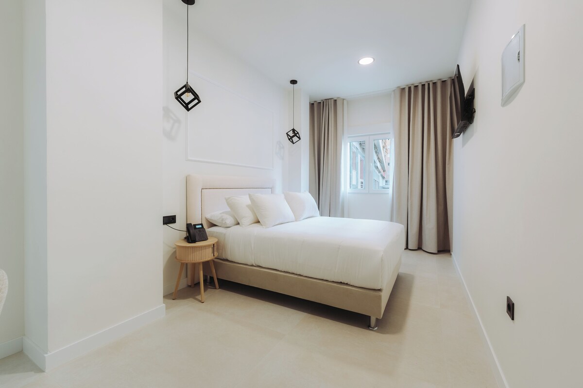 Un dormitorio moderno con cama, mesita de noche y televisor montado en la pared.
