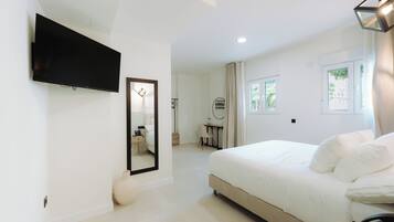 A modern hotel room with a large bed, a flat-screen TV, a desk with a chair, and a bathroom in the background.