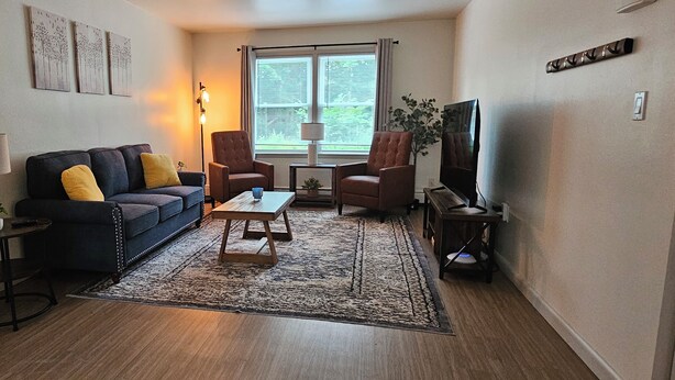 Ein Wohnzimmer mit einem dunkelblauen Sofa, zwei Sesseln, einem Couchtisch und einem Fernseher.