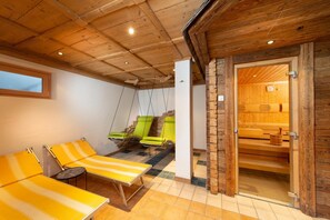 Ein Spa-Raum mit Holzbalkendecke, Steinwand und einer Sauna, die durch eine offene Tür sichtbar ist.
