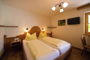 A bedroom with two beds, a nightstand, a chair, a TV, and a ceiling light fixture. - Das Jagdhaus im Großarltal (Großarl)