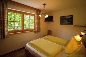 Ein Zimmer mit zwei Betten, einem Fernseher auf einem Regal, einem Gemälde an der Wand und einem Fenster mit Vorhängen.