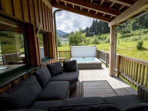 A wooden deck with a sofa and a hot tub, overlooking a green landscape. - One-bedroom Cabin (Sankt Georgen am Kreischberg)