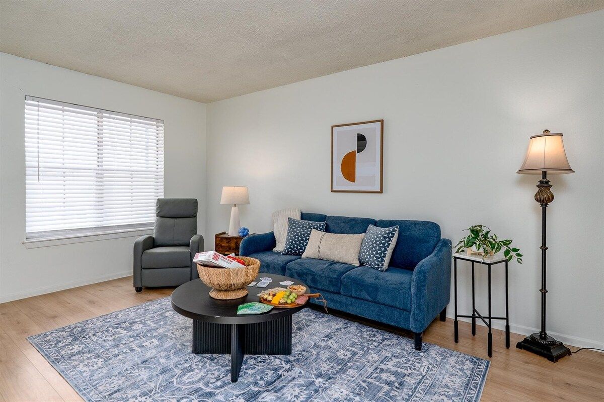 A living room with a blue sofa, a grey armchair, a coffee table with a basket, and a floor lamp.