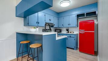 A kitchen with blue cabinets, a red refrigerator, and two wooden stools.