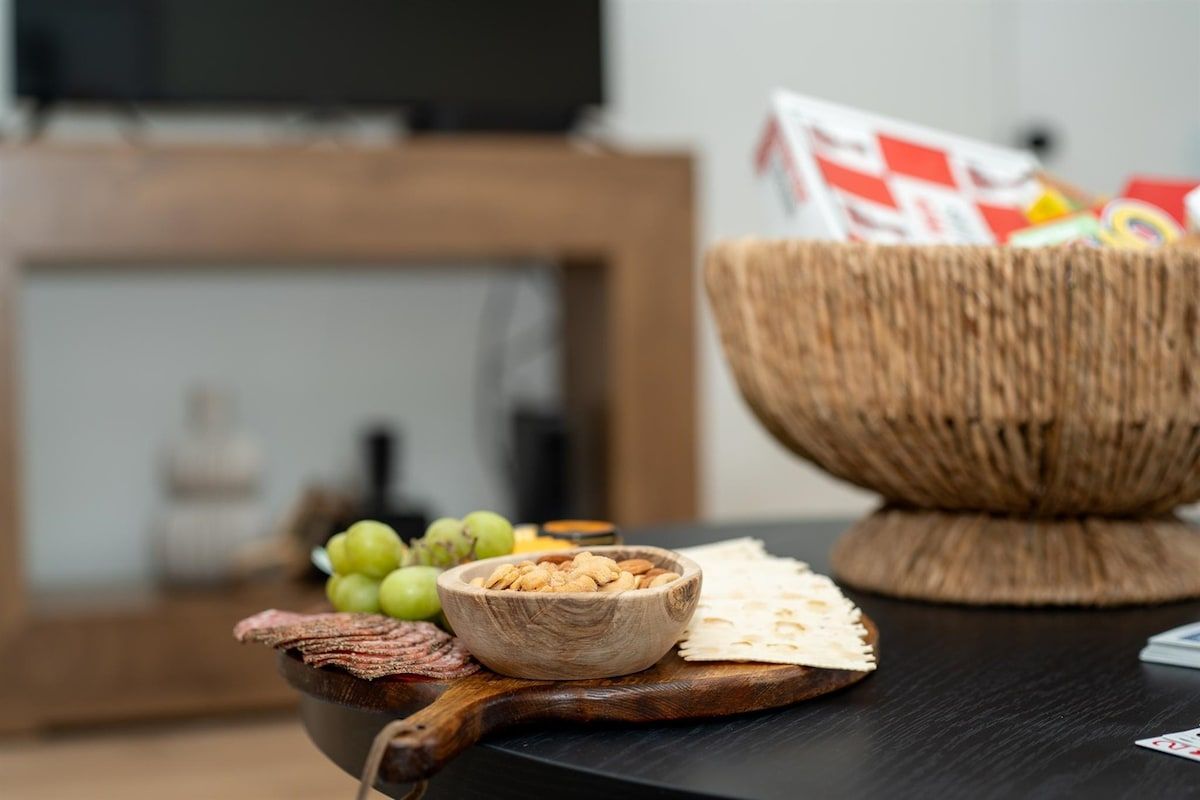 A wooden bowl filled with almonds and a small bowl of grapes on a dark wooden table.