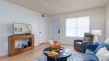 Un salon comprenant un canapé, une table basse avec un panier, une console sur laquelle est posé un panneau, et une porte.