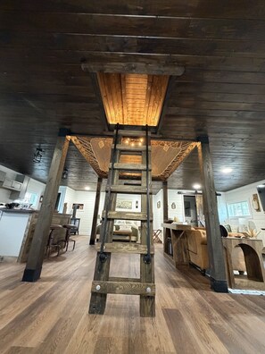 A wooden interior with a central wooden staircase, a kitchen area, and a dining space.