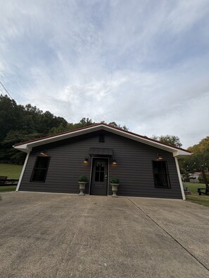 A two-story building with a dark facade, a red roof, and a front door. There are two potted plants on either side of the door.