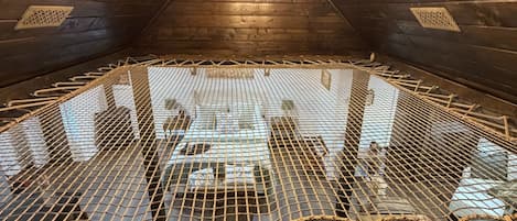 A high-ceilinged room with wooden walls and a netted floor, featuring a chandelier and a view through the netting.