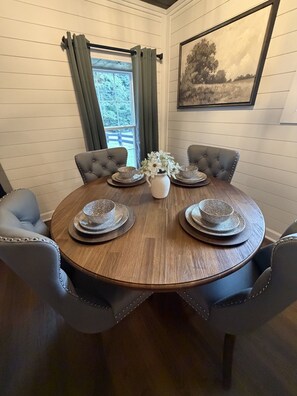A round dining table with a wooden finish, surrounded by six upholstered chairs with a tufted design.