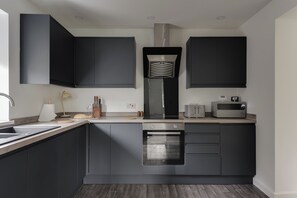 A modern kitchen with dark cabinetry, a built-in oven, a microwave, and a range hood. - Contractors | 3BDR | Parking | Near Universal (Brogborough)