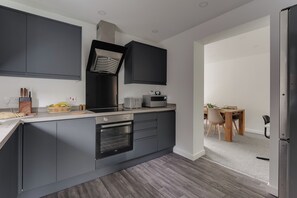 A modern kitchen with dark cabinetry, a built-in oven, and a dining area with a wooden table and chairs. - Contractors | 3BDR | Parking | Near Universal (Brogborough)