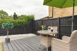 A patio with a round table and wicker chairs, a small potted tree, and a bottle of wine.