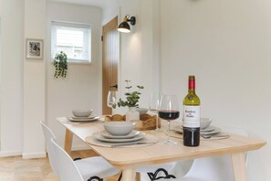Taula de dinar coberta amb plats, bols i una ampolla de vi, amb una finestra i una planta al fons.