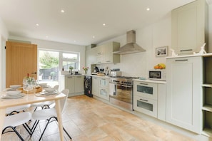 A modern kitchen with a dining area, featuring a stove, oven, and washing machine. - Luxury 2-Bed House in Stevenage Sleeps 6 Free Parking Barefoot & Board (Shephall)