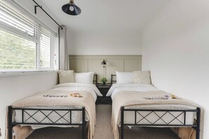 A room with two single beds, a nightstand with a lamp, and a window with blinds.