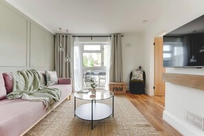 A living room with a sofa, a round coffee table, a television, and a view of the outdoors. - Luxury 2-Bed House in Stevenage Sleeps 6 Free Parking Barefoot & Board (Shephall)