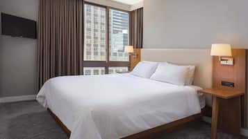 A hotel room with a large bed, a flat-screen TV mounted on the wall, a window with curtains, and a nightstand with a lamp.
