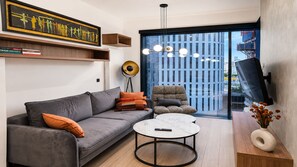 A modern living room with a grey sofa, a round coffee table, a floor lamp, and a view of a cityscape through a large window. - Apartamenty Sun&Snow w obiekcie Towarowa (Warszawa)