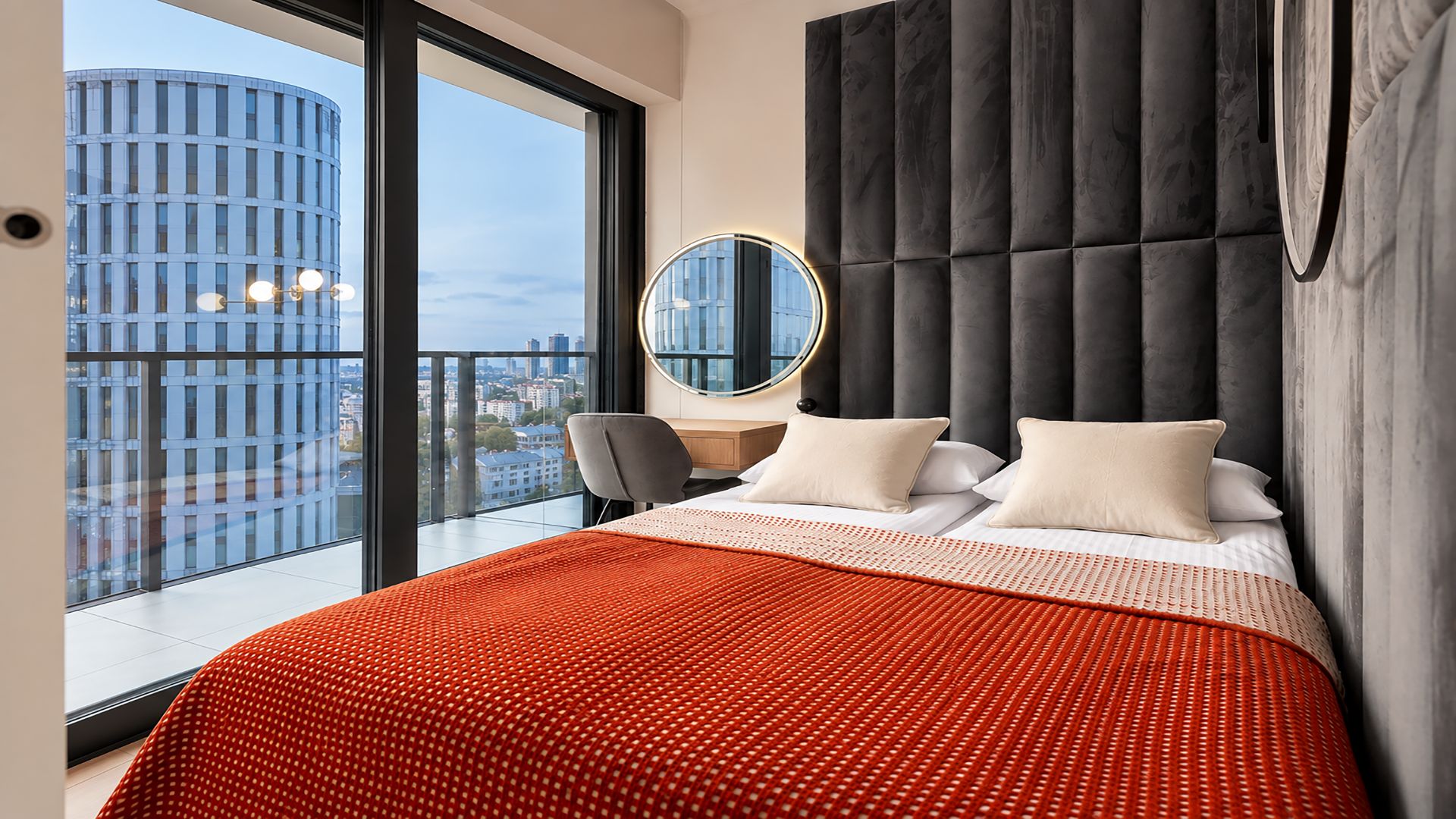 Ein modernes Hotelzimmer mit einem großen Bett, einem runden Spiegel und Blick auf die Stadt.