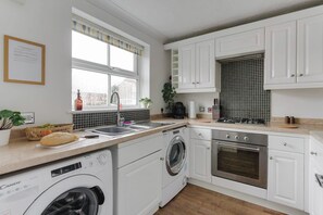 A modern kitchen with white cabinetry, a built-in washing machine, a stove, and a window with a view. - Contractors | 4BDR | Parking | Near Universal (Cranfield)