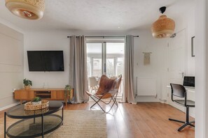 Ein modernes Wohnzimmer mit Flachbildfernseher, einem Holzschrank, einem Ledersessel, einem runden Couchtisch und einem Essbereich mit Tisch und Stühlen.