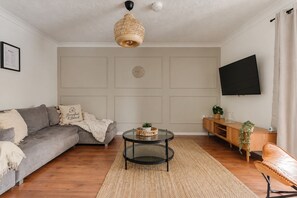 A living room with a grey sofa, a round coffee table, a wooden cabinet, and a television on the wall. - Contractors | 4BDR | Parking | Near Universal (Cranfield)