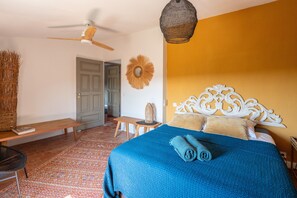 A bedroom with a bed, a ceiling fan, a woven wall hanging, and a bench.