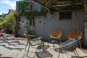 Une terrasse extérieure avec une plateforme en bois, un mur blanc orné de plantes grimpantes et deux fauteuils en osier.