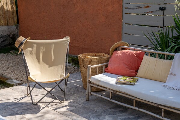 A patio area with a folding chair, a woven basket, and a sofa with cushions.