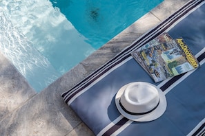 A poolside area with a magazine, a hat, and a striped towel.