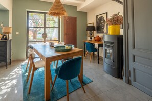 A dining area with a wooden table, blue chairs, a woven pendant light, and a view through a window to an outdoor area. - Guest Room 'Suite 55' with Wi-Fi (Tulette)