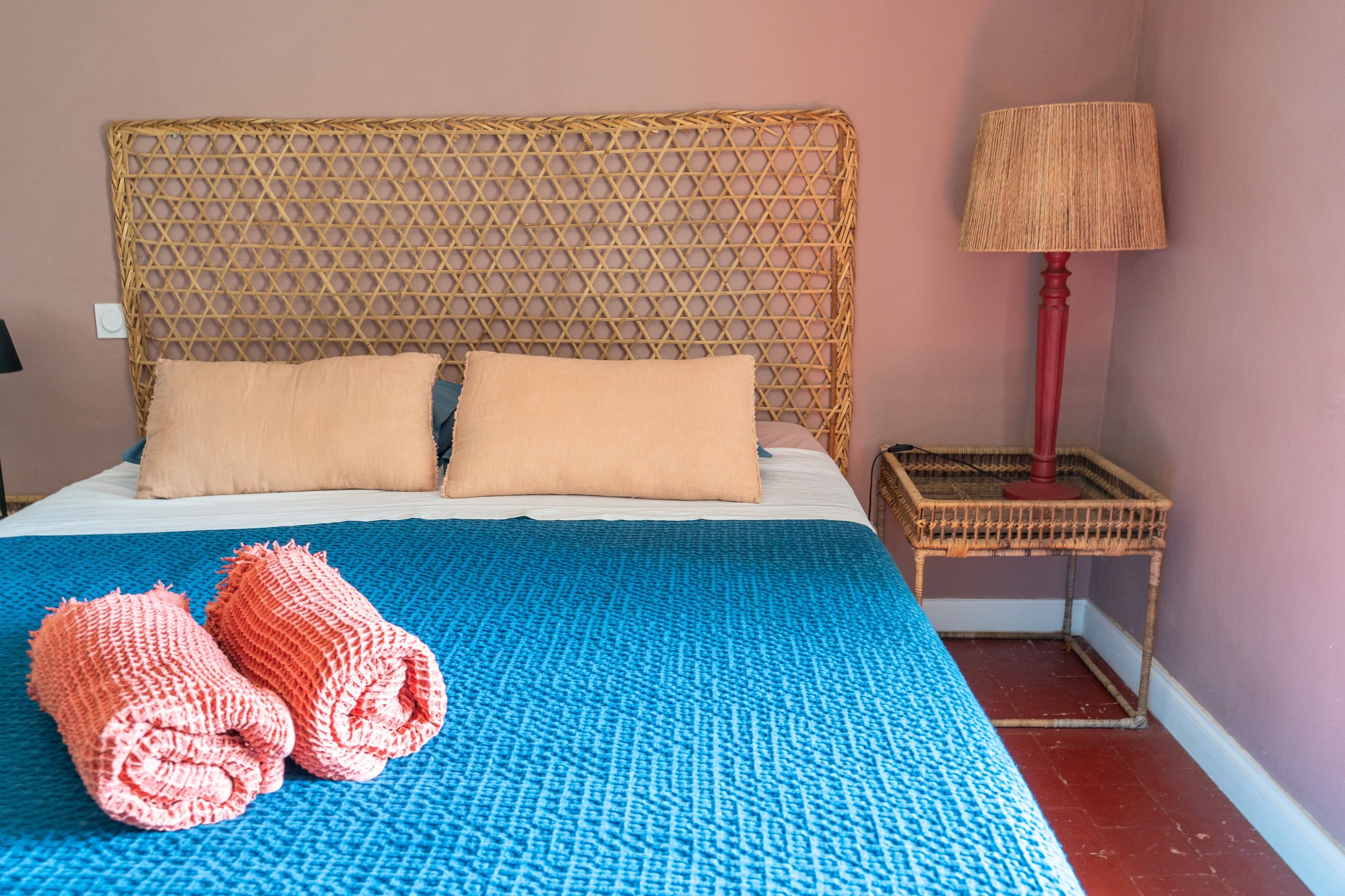 A bed with a blue blanket, two pillows, and two rolled towels.