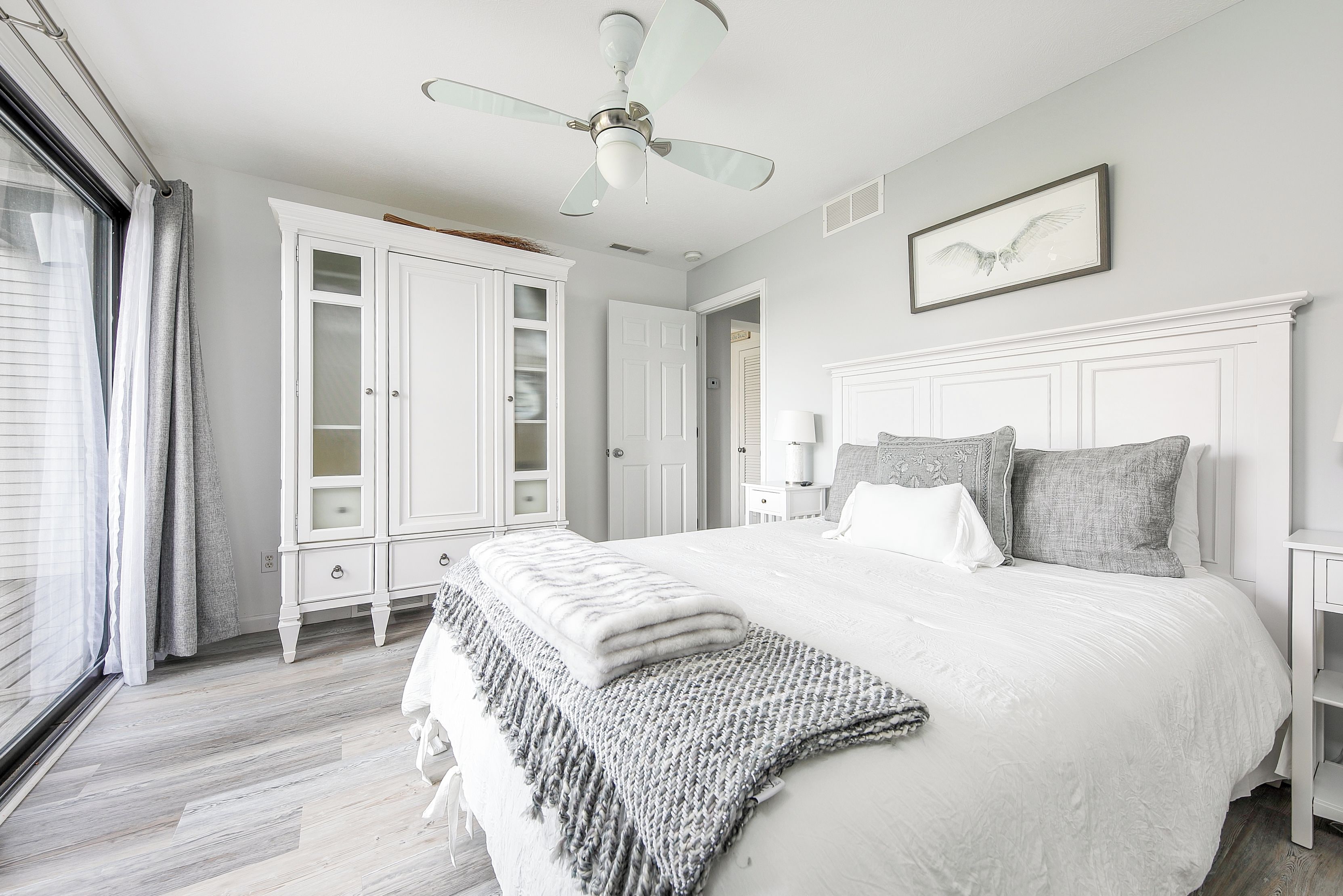 A bedroom with a bed, a ceiling fan, a wardrobe, and a window with curtains.