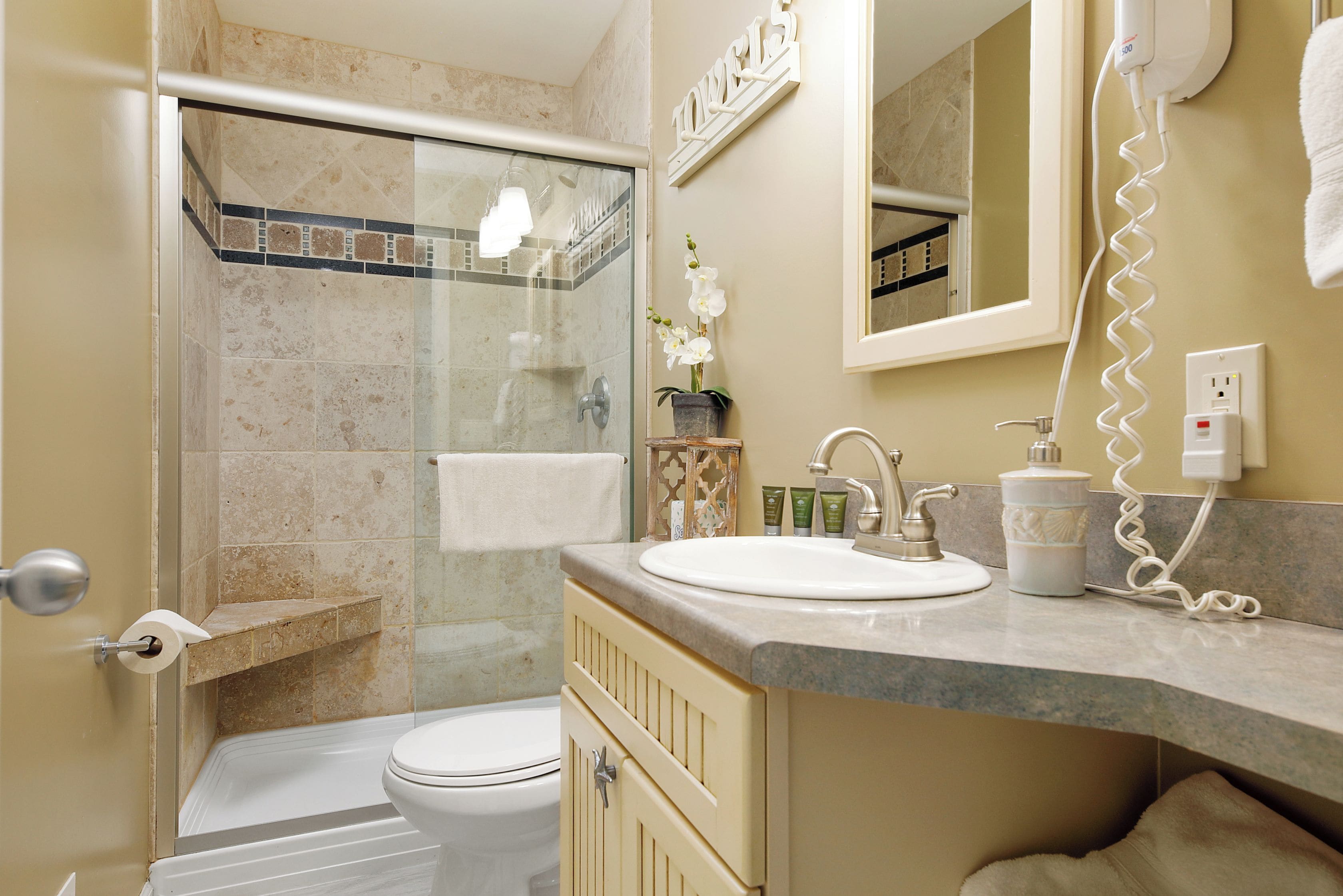 A bathroom with a shower, toilet, sink, and a hairdryer on the wall.