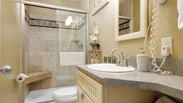 A bathroom with a shower, toilet, sink, and a hairdryer on the wall.
