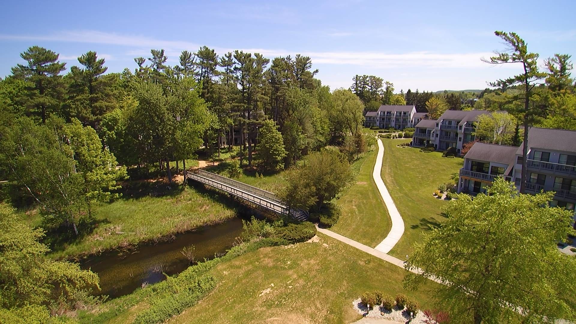 A residential area with a bridge over a stream, surrounded by trees and multi-story buildings.